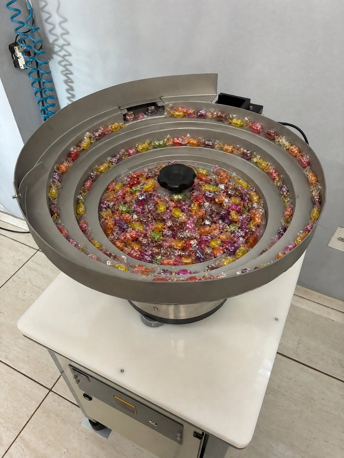 Bacia vibratória em aço inox de máquina contadora Sanick, com balas sortidas organizadas em fila única nas calhas espirais
